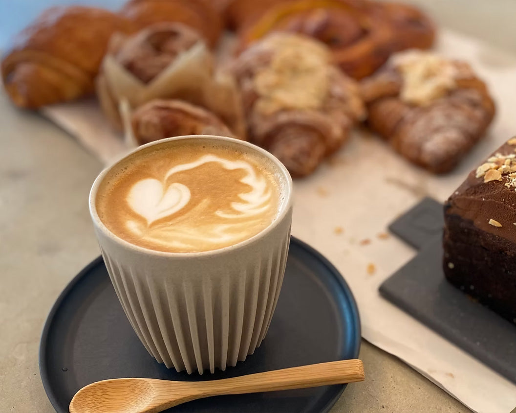 Latte in an original HuskeeCup surrounded by pastries in a cafe
