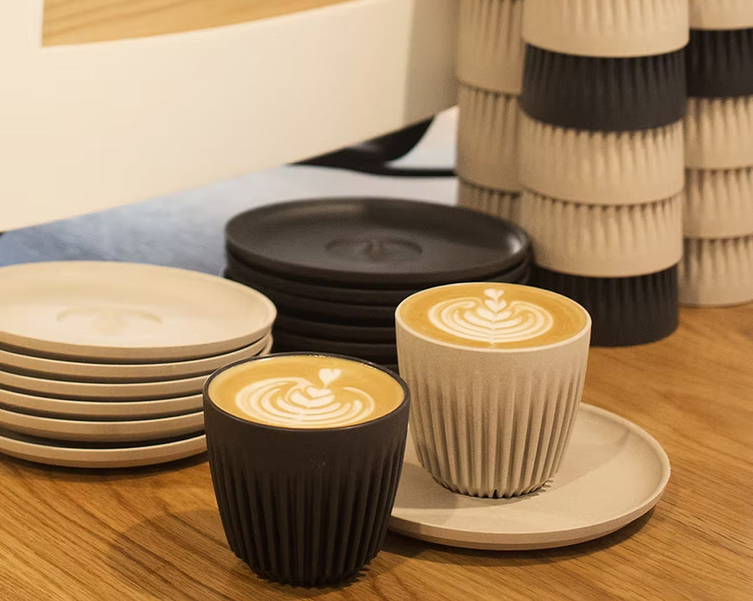 Two cups of latte with art in Original HuskeeCups with saucers and huskeecups stacked in the background